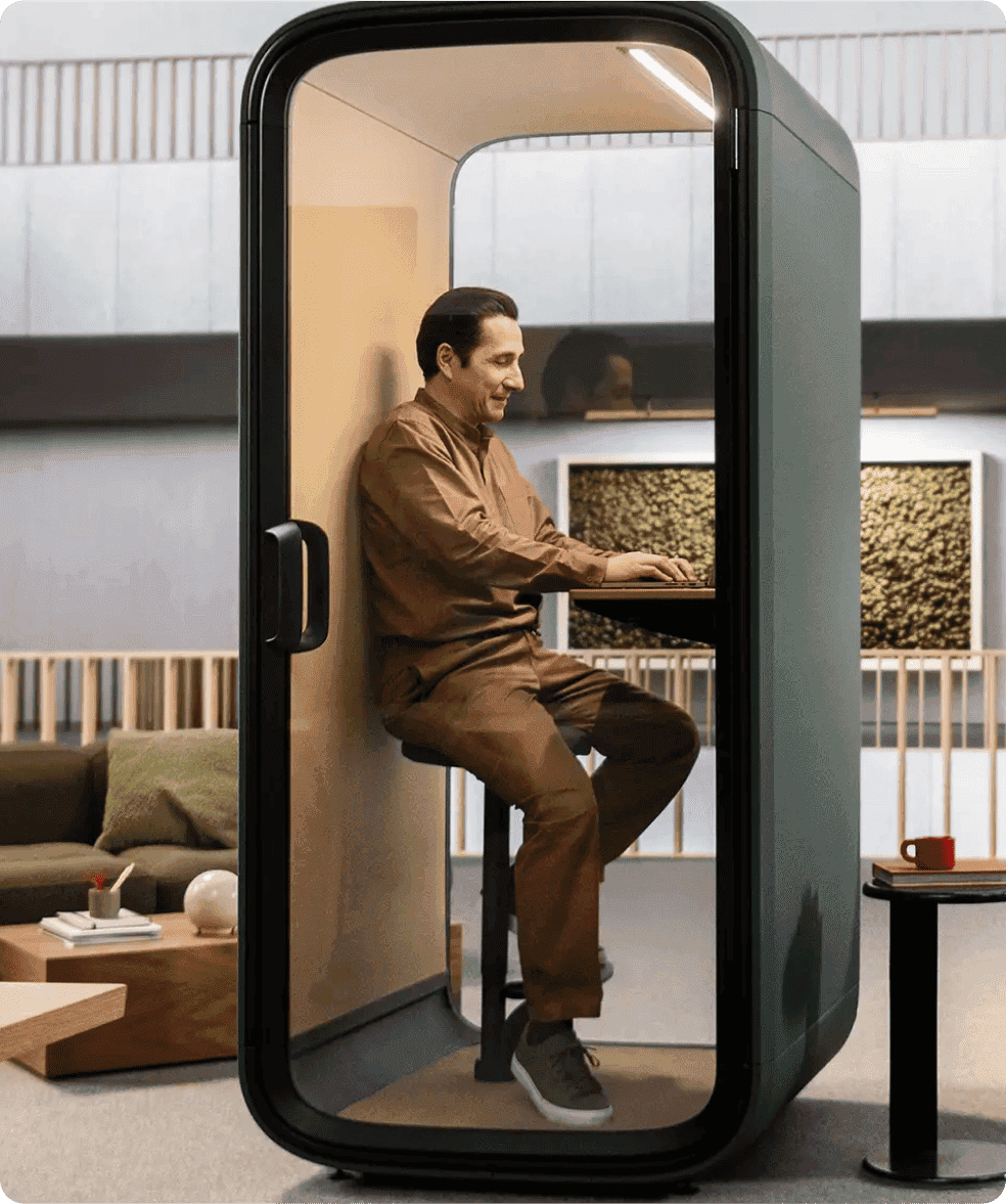 Man working on a laptop inside a private office pod in a modern workspace.